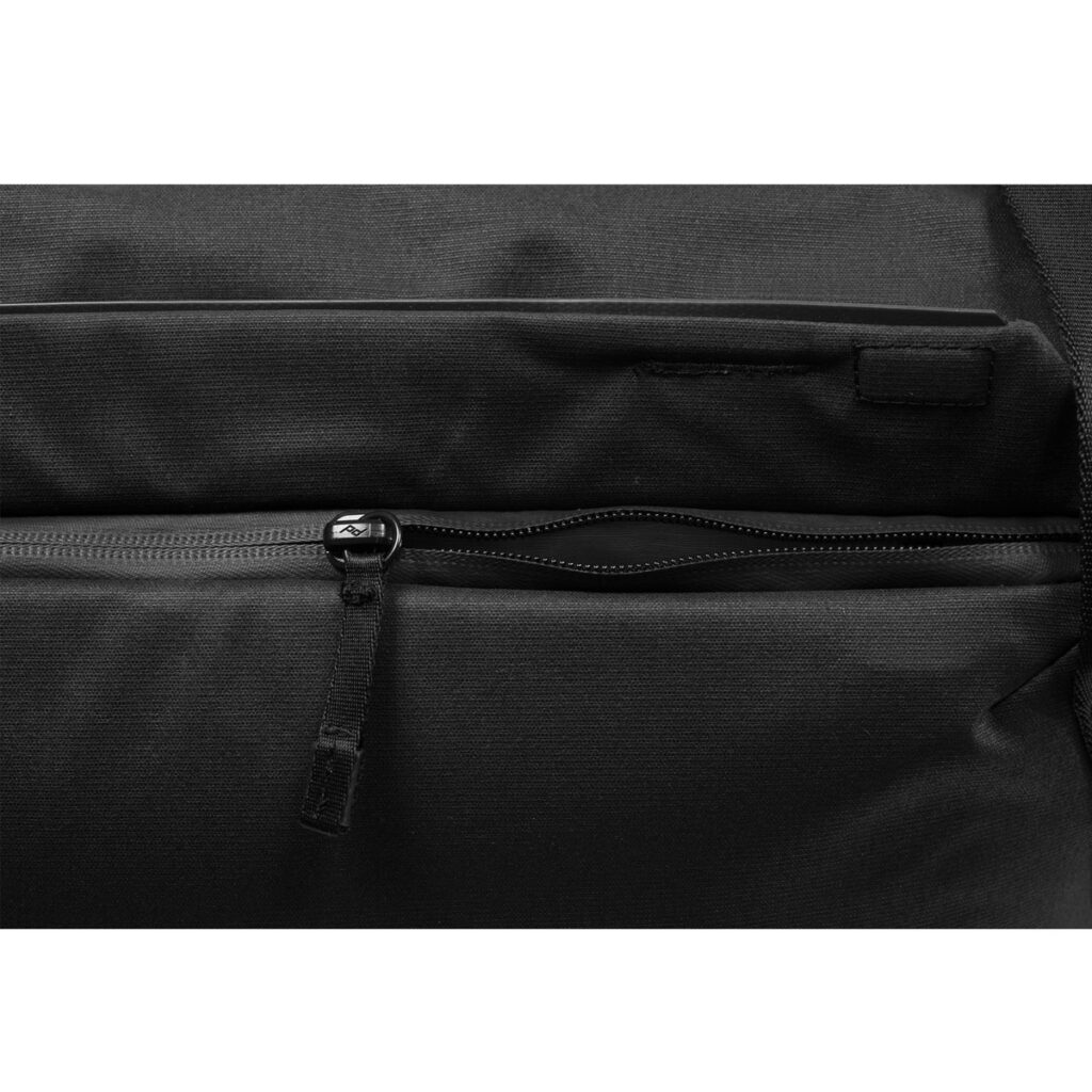 Peak-Design-Everyday-Tote-15l-black-7 Lähikuvassa Peak Design Everyday Tote 15L v2 mustana, jossa on vetoketjullinen tasku, jossa on kankainen vetokieleke läpän alla. Laukussa on sileä, kestävä rakenne.