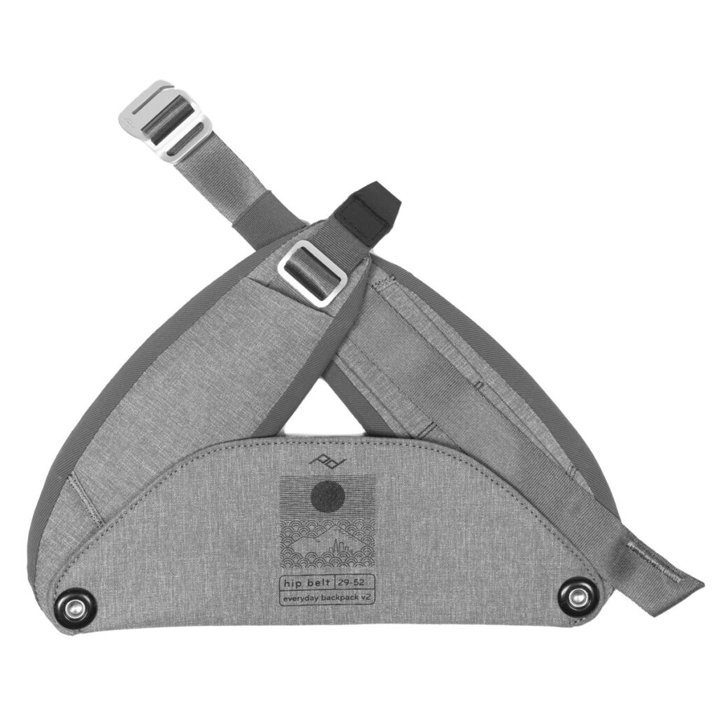 Peak-Design-Everyday-hip-belt-v2-ash-1 Peak Design Everyday Hip Belt V2 - Ash (29-52") on harmaa kangasvyö, jossa on säädettävät hihnat ja metalliset soljet ja joka on suunniteltu lisäämään repun tukea ja mukavuutta. Etiketissä on tuotetiedot ja logot pinnassa.