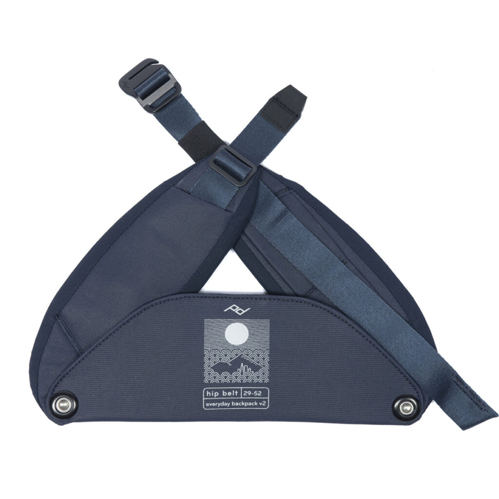 Peak-Design-Everyday-hip-belt-v2-midnight-1 Midnight navy Peak Design Everyday Hip Belt V2 (29-52") -repussa on säädettävät hihnat, metalliset napit ja etiketti, jossa on vuoristo- ja aurinkografiikkaa ja jossa lukee "hip belt p-p-52 everyday backpack v2".