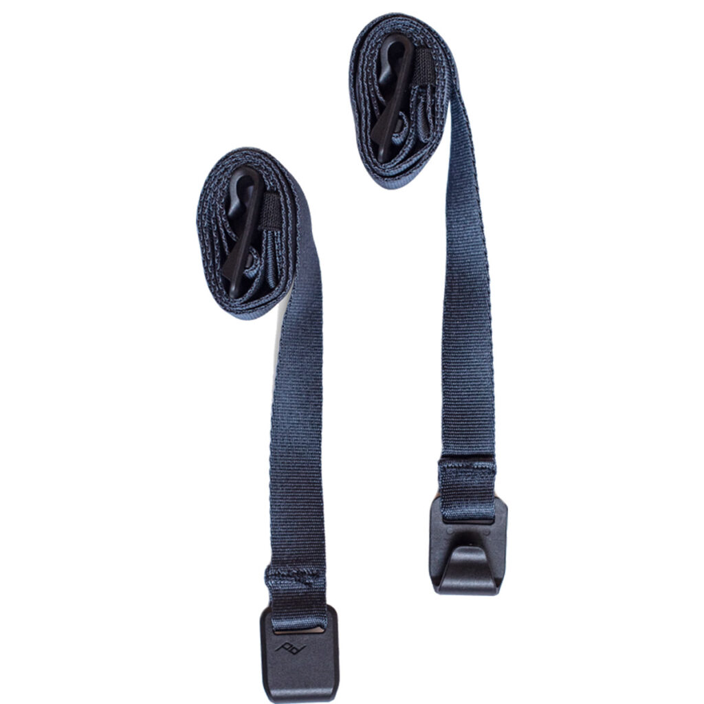 Peak-Design-External-Carry-Strap-V2-long-midnight-1 Kaksi Peak Design Spareparts V2 -ulkoista kantohihnaa (pitkä, Midnight), joissa on muovisoljet, ovat osittain rullattuina ja makaavat yhdensuuntaisesti valkoisella pohjalla; soljet on kiinnitetty toiseen päähän, ja toiset päät on kääritty ylös.