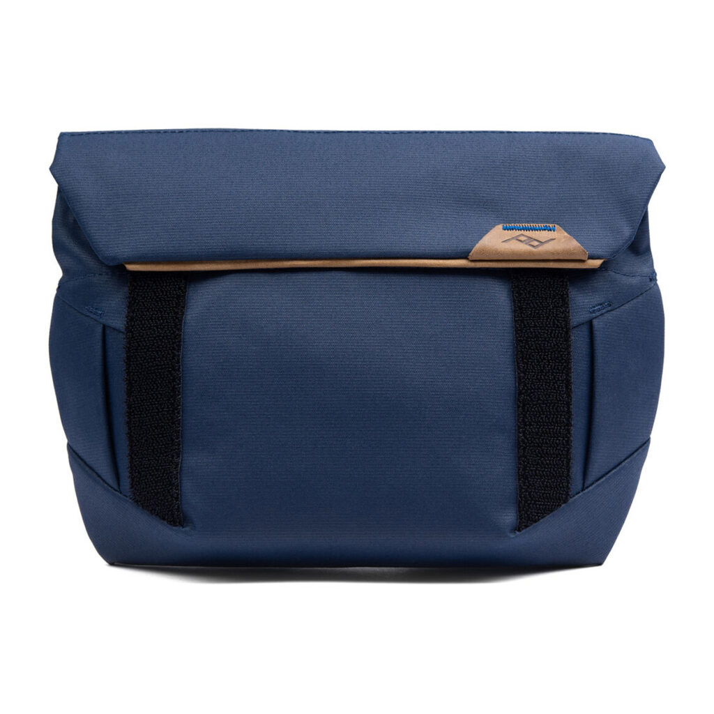 Peak-Design-Field-Pouch-V2-midnight-2 Peak Design Field Pouch V2 - Midnight on sininen kangaslähettilaukku, jossa on ruskehtavat korostukset, mustat pystysuorat hihnat, läppäsuljenta, minimalistinen muotoilu ja pieni ommeltu logo lähellä läpän yläreunaa.