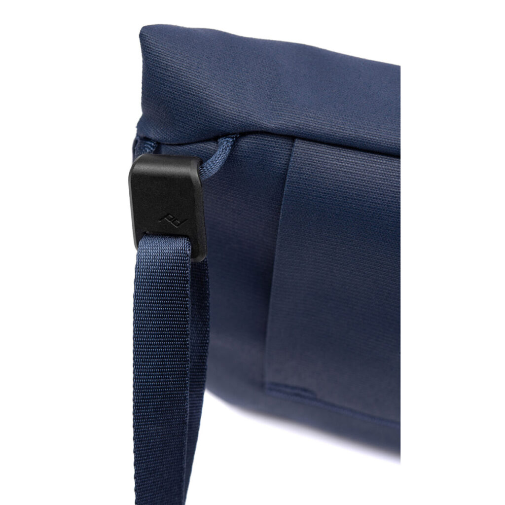 Peak-Design-Field-Pouch-V2-midnight-6 Lähikuva Peak Design Field Pouch V2 - Midnight -laukusta, jossa näkyy kulma, jossa on musta muovinen hihnalukko ja kiinnitetty hihna, ja jossa korostuu tummansinisen kankaan rakenne ja yksityiskohtaiset ompeleet.