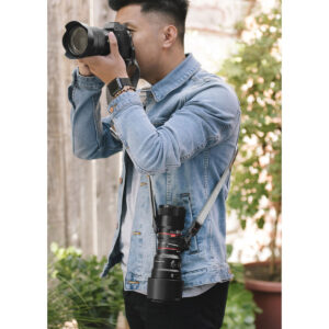 Vaaleansiniseen farkkutakkiin pukeutunut henkilö käyttää Peak Design Lens Kit - Canon EF -objektiivisarjaa valokuvien ottamiseen, kun toinen kamera roikkuu hänen kaulassaan. Taustalla näkyy vihreitä kasveja ja puinen aita.
