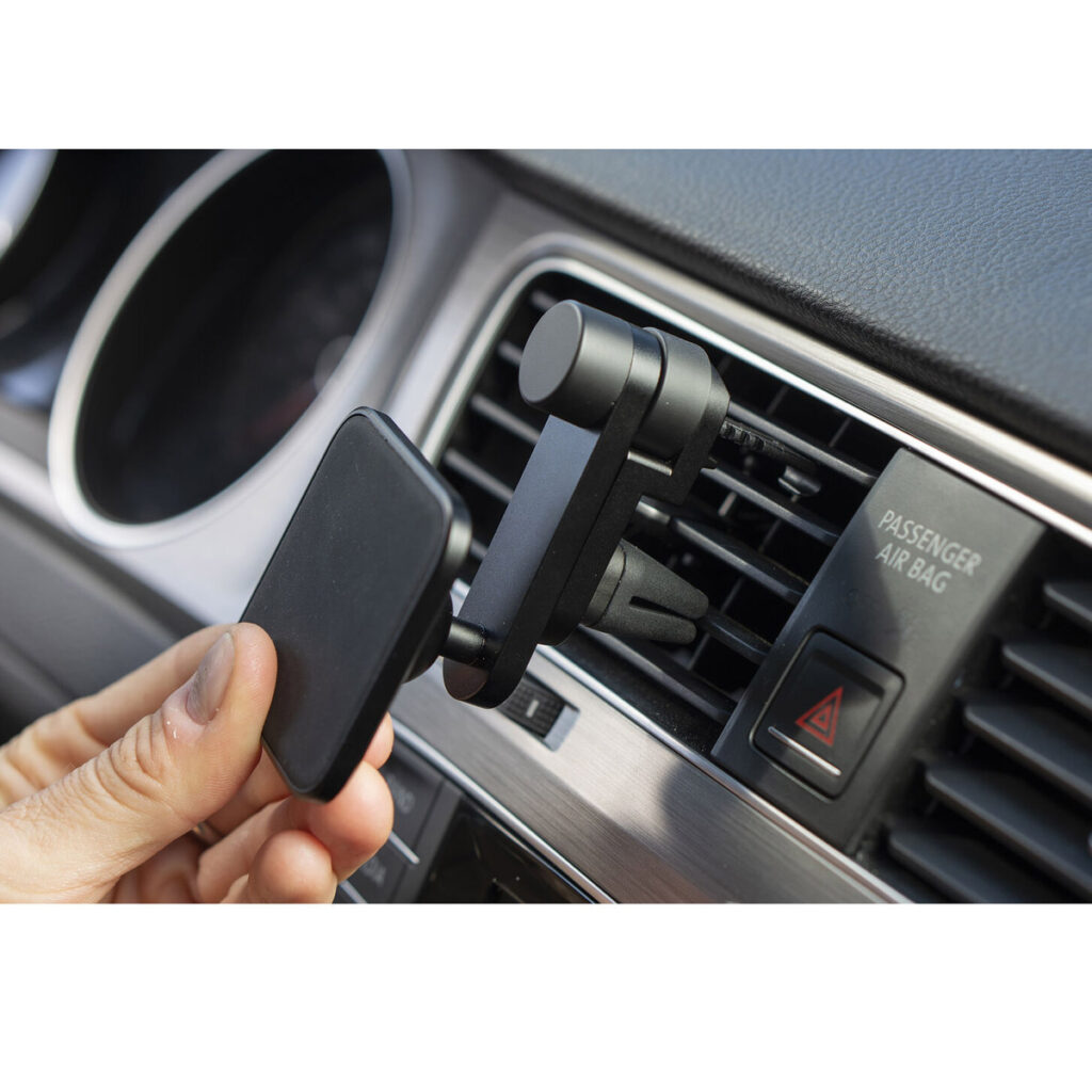 Käsi kiinnittää Peak Design Mobile Charging Car Mount Vent -musteen, mustan magneettipuhelimen pidikkeen, auton tuuletusaukkoon kojelaudan lähelle, matkustajan turvatyynyn merkkivalon ja hätävilkun painikkeen viereen.