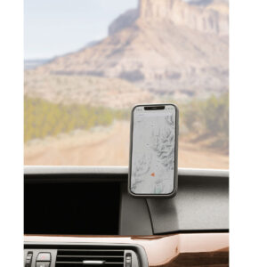 Peak-Design-Mobile-Magnetic-Car-Mount5 Peak Design Mobile VHB-tarra-autotelineessä on älypuhelin, joka näyttää kartan auton kojelaudalla, ja taustalla näkyy tuulilasin läpi sumea kalliomaisema ja hiekkatie.