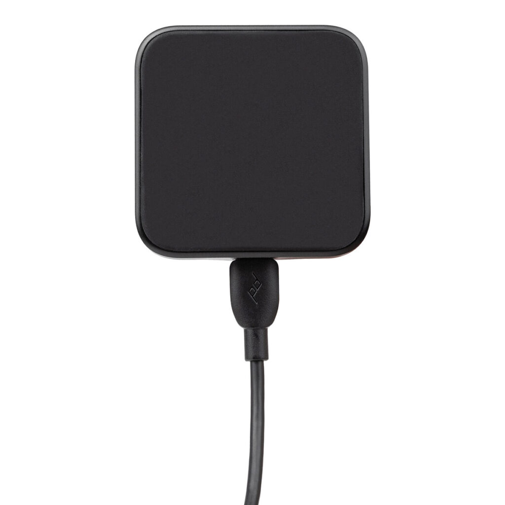 Peak-Design-Mobile-Magnetic-Charging-Car-Mount3 Peak Design Mobile VHB-tarra latausautotelineessä, joka näkyy ylhäältäpäin mustana ja jossa on pyöristetyt neliönmuotoiset kulmat, on latauskaapeli kytkettynä keskellä alhaalla valkoista taustaa vasten.