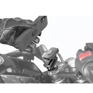 Peak-Design-Mobile-Motorcycle-Stem-Mount-4 Käsi pitää älypuhelinta moottoripyörän ohjaustangon yläpuolella, kun se aiotaan kiinnittää Peak Design Mobile Motorcycle Stem Mount -malliin, ja kiinnike ja pyörän hallintalaitteet ovat selvästi näkyvissä.