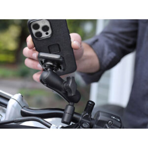 Peak-Design-Mobile-Motorcycle-ball-adapter-5 Henkilö kiinnittää mustalla kotelolla varustetun älypuhelimen Peak Design Mobile Motorcycle Mount 1" Ball Adapteriin pyöräänsä tai moottoripyöräänsä ulkona.
