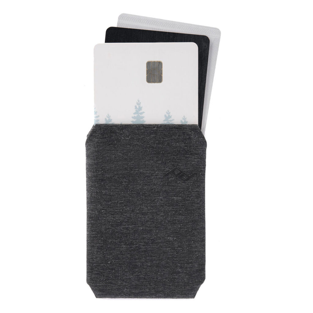 Peak-Design-Mobile-Wallet-Slim-3 Peak Design Mobile Wallet Slim - Charcoal -lompakko on harmaata kangasta, ja siinä on kolme osittain näkyvää korttia - yksi, jossa on siru ja heikko puumalli - valkoista taustaa vasten.