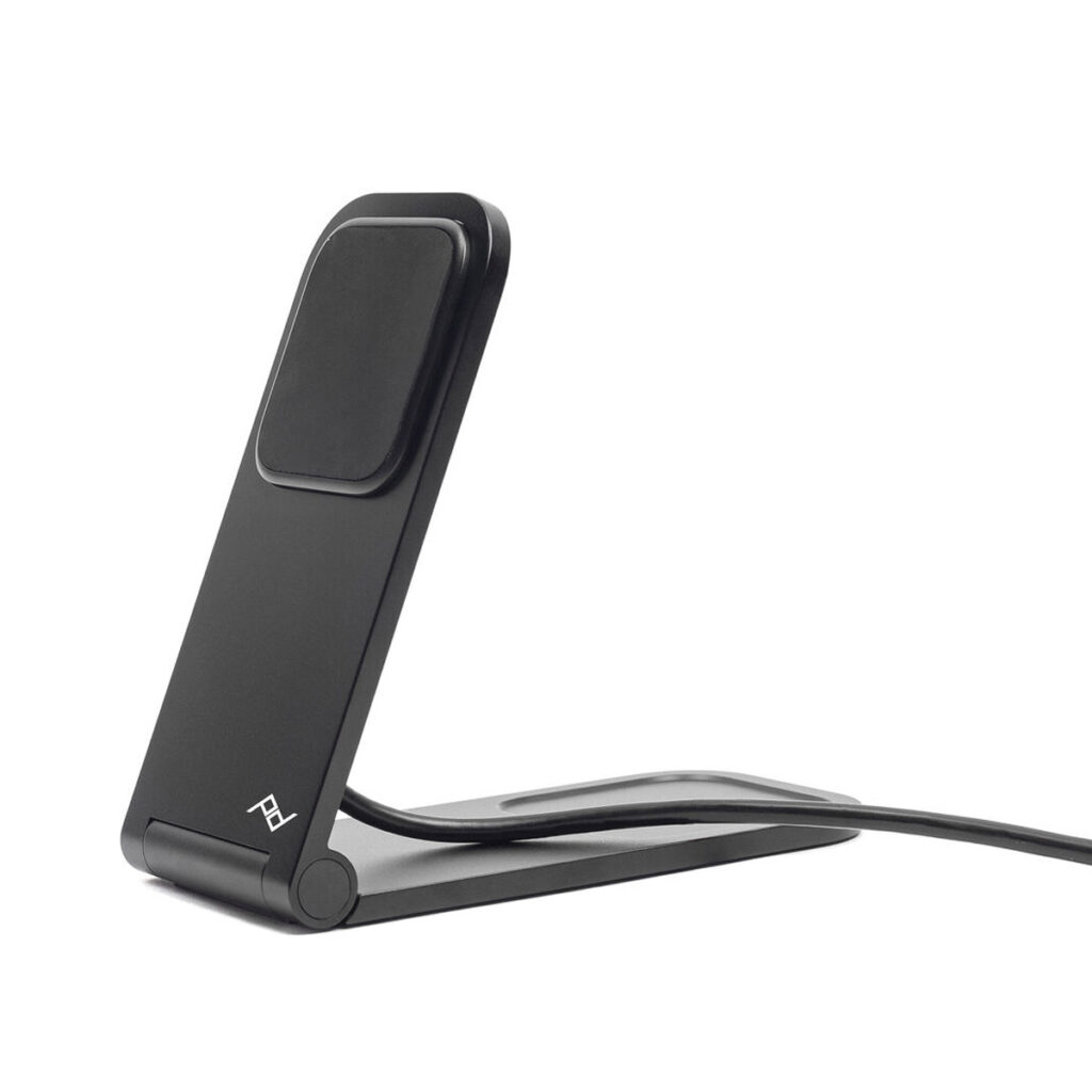 Peak-Design-Mobile-Wireless-Charging-Stand-2 Peak Design Mobile Wireless Charging Stand on tyylikäs ja musta, ja siinä on kulmikas muotoilu, jossa on litteä latausalusta ja liitetty kaapeli, ja se on sijoitettu valkoista taustaa vasten.