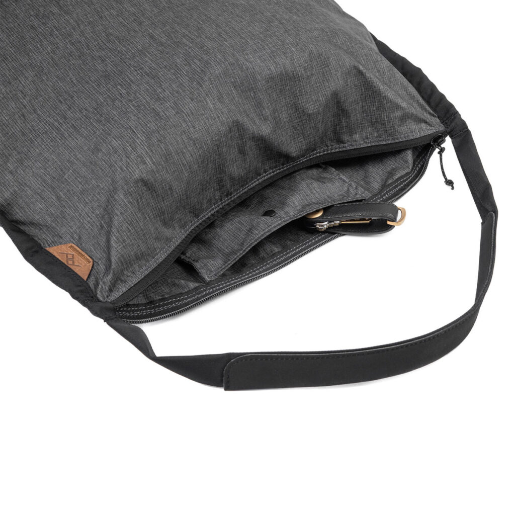 Peak-Design-Packable-Tote---Charcoal3 Lähikuva Peak Design Packable Tote in Charcoal, jossa on musta säädettävä hihna, osittain auki vetoketju näyttää sisätasku ja ulkopuolinen nahka laastari.