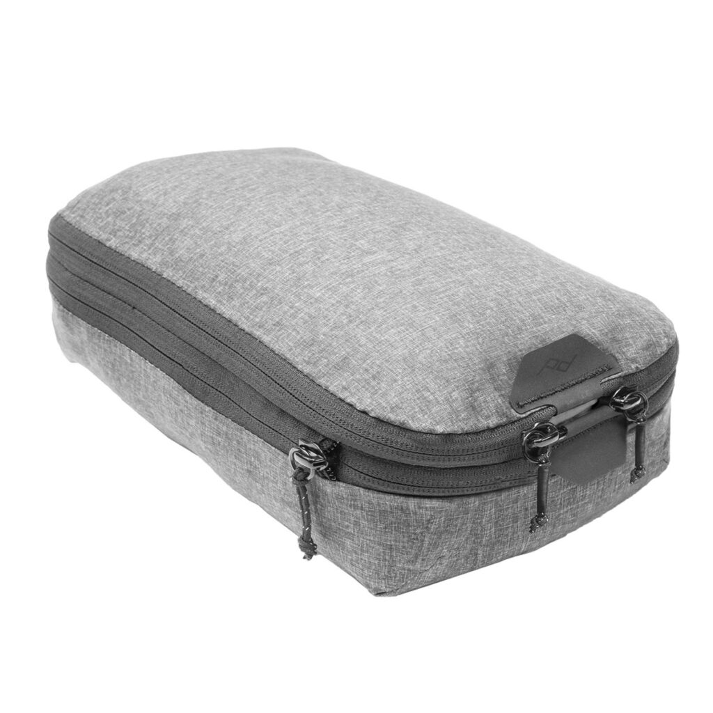 Peak-Design-Packing-Cube-Small---Charcoal1 Peak Design Packing Cube Small - Charcoal on harmaasta kankaasta valmistettu vetoketjullinen pussi, jossa on kaksi päälokeroa, neljä vetoketjuvetoketjua ja minimalistinen muotoilu, jossa on pieni kulmalogo - ihanteellinen tavaroiden järjestämiseen.