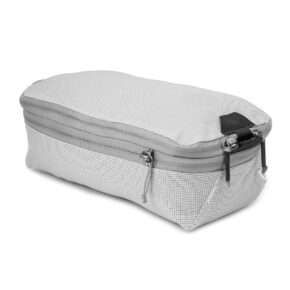 Peak Design Packing Cube Small - Raw on vaaleanharmaa, suorakulmainen matkapussi, jossa on kuvioitu kuvio, kaksi vetoketjun vetoketjua ja pieni musta logolappu toisessa päässä.