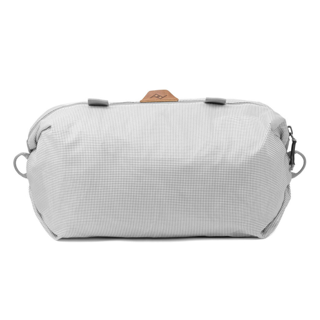 Peak-Design-Shoe-Pouch---Raw1 Peak Design Shoe Pouch - Raw on vaaleanharmaa vetoketjullinen pussi, jossa on kuvioitu kuvio, kaksi sivulenkkiä ja pieni ruskea aksenttilappu päällä valkoisella pohjalla.