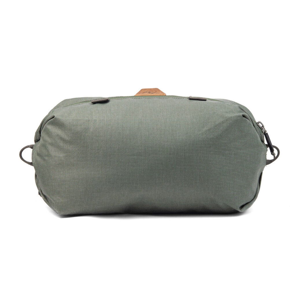 Peak-Design-Shoe-Pouch---Sage1 Peak Design Shoe Pouch in Sage on suorakulmainen matkalaukku, jossa on kuvioitu kangas, musta vetoketju ja sivulenkit, kuvassa valkoista taustaa vasten.