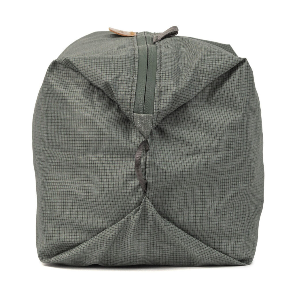 Peak-Design-Shoe-Pouch---Sage2 Peak Design Shoe Pouch in Sage on vihreä, suorakaiteen muotoinen kangaspussi, jossa on ruudukkokuvio, vetoketju edessä ja hieman ryppyinen viimeistely, ja se on kuvassa pystyssä valkoisella pohjalla.