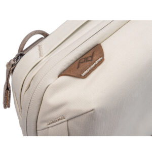 Peak-Design-Tech-Pouch-Bone-3 Lähikuva Peak Design Tech Pouch - Bone -laukusta, joka on beige kangasorganisaattori, jossa on ruskea nahkainen aksentti, jossa on PD-logo, vetoketju, jossa on kangasvetoketju ja yksityiskohtaiset ompeleet.