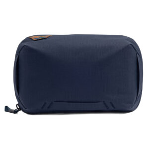 Peak-Design-Tech-Pouch-Midnight-1 Peak Design Tech Pouch - Midnight on laivastonsininen suorakulmainen matkapussi, jossa on vetoketju ja pieni ruskea laastari vasemmassa yläkulmassa valkoista taustaa vasten.
