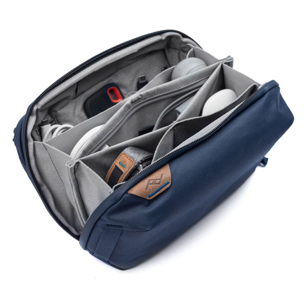 Peak-Design-Tech-Pouch-Midnight-2 Peak Design Tech Pouch - Midnight -laukussa, joka on kuvassa avattuna, järjestetään siististi kaapelit, vempaimet ja tarvikkeet, kuten kuulokkeet, laturi ja USB-asema, sen useisiin lokeroihin.