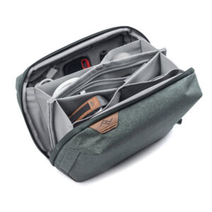Peak-Design-Tech-Pouch-Sage-2 Peak Design Tech Pouch - Sage on osittain auki ja paljastaa järjestetyn säilytystilan tarvikkeille useissa pehmustetuissa lokeroissa ja väliseinissä, joiden etupuolella on näkyvissä nahkalaikka, jossa on logo.