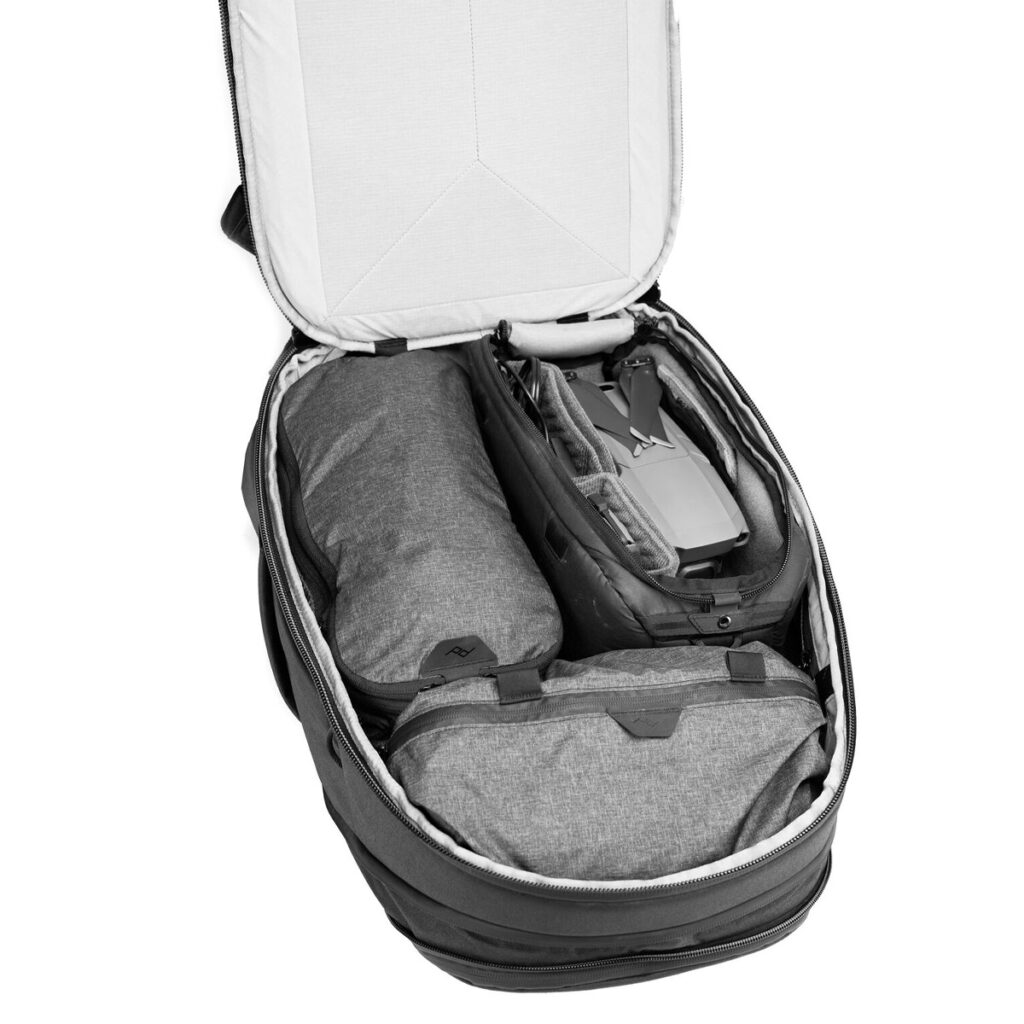 Peak-Design-Travel-Backpack-30L-black4 Peak Design Travel Backpack 30L -kamerareppu (musta) on auki, ja siinä näkyy siististi järjestettyjä osioita, joiden sisällä on pakattuja esineitä - rullattu takki tai pussi, drone ja toinen vetoketjullinen lokero.