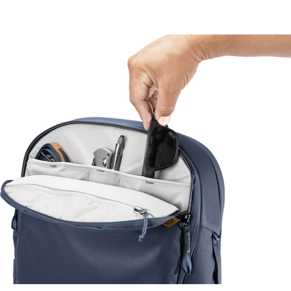 Peak-Design-Travel-Backpack-30L-midnight5 Käsi liu'uttaa aurinkolasit Peak Design Travel Backpack 30L -kamerareppu, tummansininen -matkarepun etulokeron sisällä olevaan järjestettyyn taskuun kynän, lyijykynän ja avainten viereen.