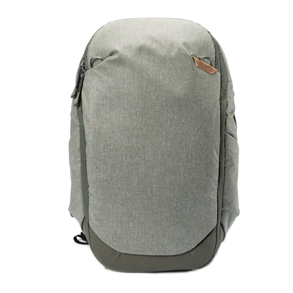 Peak-Design-Travel-Backpack-30L-sage2 Vaaleanvihreässä Peak Design Travel Backpack 30L -kamerareppu on minimalistinen, strukturoitu malli, jossa on vetoketjullinen etutasku ja pieni ruskea korostus, joka näkyy pystyssä valkoista taustaa vasten.