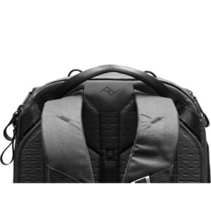 Peak-Design-Travel-Backpack-45L-black05 Lähikuva Peak Design Travel Backpack 45L -kamerareppu, musta, jossa korostuvat sen pehmustetut olkahihnat, tukeva kahva ja geometrinen logo takapaneelissa valkoista taustaa vasten.