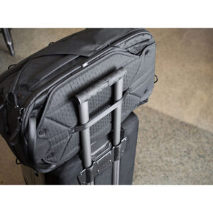Peak-Design-Travel-Backpack-45L-black08 Peak Design Travel Backpack 45L -kamerareppu, musta on kiinnitetty tukevasti rullalaukun teleskooppikahvaan, joka lepää pilkullisella lattialla.