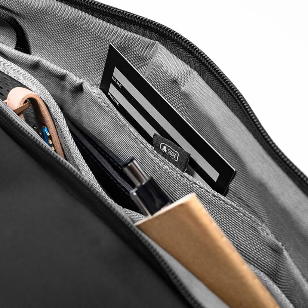 Peak-Design-Travel-Duffel-35l-black-5 Lähikuva Peak Design Travel Duffel 35L - Black -mallin järjestäytyneestä sisätilasta, jossa kynät, muistikirja, latauskaapelit ja mustavalkoinen kortti ovat siististi erillisissä lokeroissa.