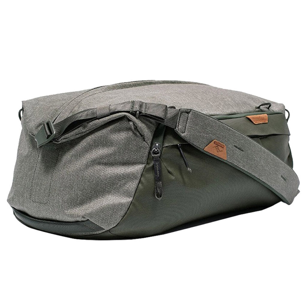 Peak-Design-Travel-Duffel-35l-sage-4 Peak Design Travel Duffel 35L Sage -mallistossa on harmaan ja tummanvihreän sävyjä, leveä säädettävä olkahihna, vetoketjulokeroita ja ruskea logolaastari sivulla valkoista taustaa vasten.