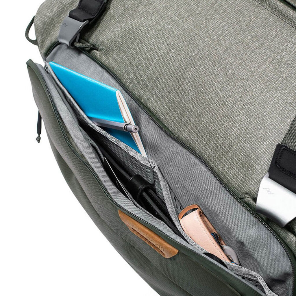 Peak-Design-Travel-Duffel-35l-sage-5 Peak Design Travel Duffel 35L - Sage näkyy avattuna, ja siitä paljastuu järjestettyjä lokeroita, joiden sisällä on siististi sininen muistikirja, kynä, älypuhelin ja beige laukku.