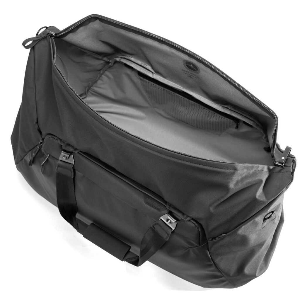 Peak-Design-Travel-Duffel-65l-black-2 Peak Design Travel Duffel 65L - Black on esitetty avattuna ylhäältä päin, jolloin sen tilava päälokero ja vetoketjullinen verkkotasku ovat näkyvissä. Laukussa on tukevat kahvat ja tyylikäs, moderni muotoilu.