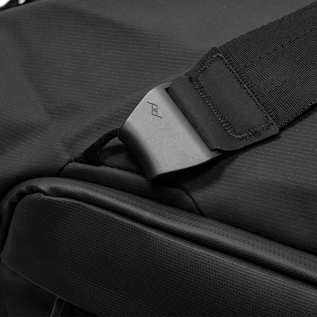 Peak-Design-Travel-Duffel-65l-black-5 Lähikuva Peak Design Travel Duffel 65L -matkakassista, musta, jossa on pehmustettu olkahihna, muovisolki, jossa on pd-kaiverrus, ja jossa näkyy sen kuvioitu, kestävä materiaali ja tukeva rakenne.