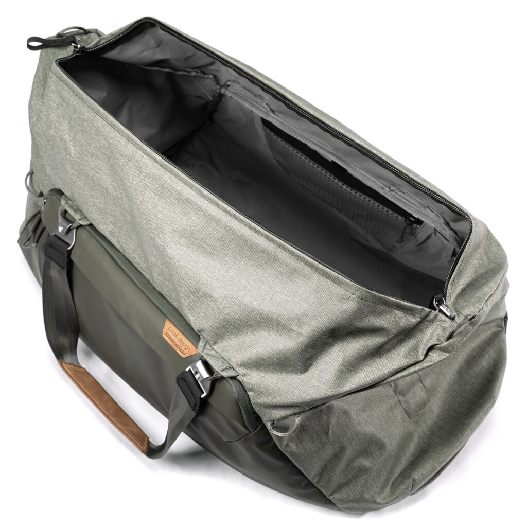 Peak-Design-Travel-Duffel-65l-sage-2 Peak Design Travel Duffel 65L - Sage on tilava, avoin harmaan ja vihreän värinen laukku, jossa on mustat hihnat, ruskea nahkakahva-aksentti ja tyhjä päälokero kuvattuna ylhäältä katsottuna.