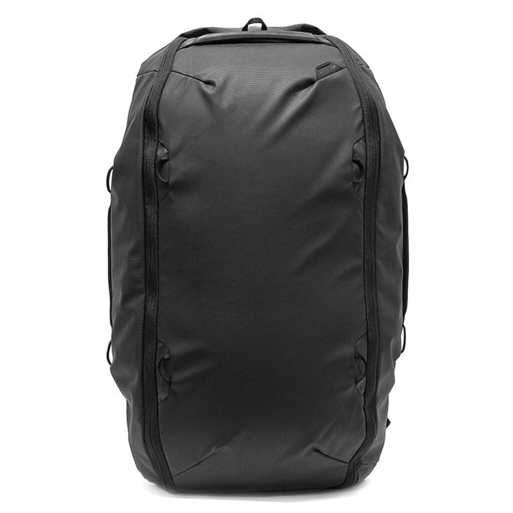 Peak-Design-Travel-Duffelpack-65l-black-01 Mustassa Peak Design Travel Duffelpack 65L -matkarepussa on minimalistinen, pyöristetty muotoilu, jossa on useita kahvoja ja vetoketjuja valkoista taustaa vasten.