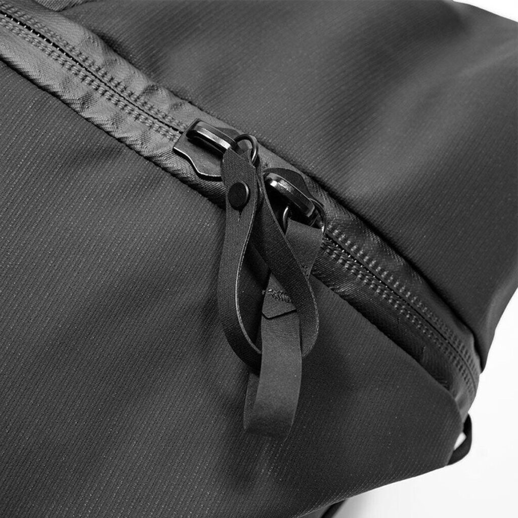 Peak-Design-Travel-Duffelpack-65l-black-06 Lähikuva Peak Design Travel Duffelpack 65L - Black -repun mustasta vetoketjusta, jossa on nahkainen vetokieleke ja kuvioitu kangas.