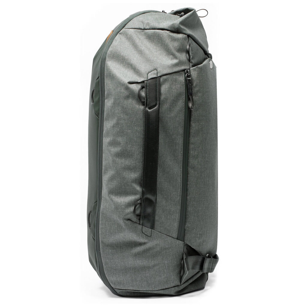 Peak-Design-Travel-Duffelpack-65l-sage-3 Peak Design Travel Duffelpack 65L Sage -mallistossa on tyylikäs ja moderni muotoilu mustilla vetoketjuilla ja kahvoilla, useilla lokeroilla ja tukevalla kankaalla. Kuvattu pystyasennossa valkoista taustaa vasten.