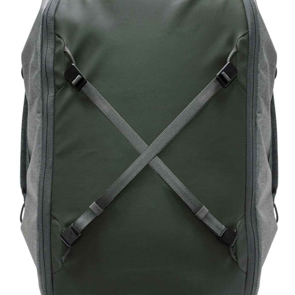 Peak-Design-Travel-Duffelpack-65l-sage-4 Lähikuva Peak Design Travel Duffelpack 65L Sage -mallistosta, jossa on kaksi säädettävää harmaata hihnaa, jotka risteävät X-muodossa edessä, ja jossa on minimalistinen ja moderni muotoilu.