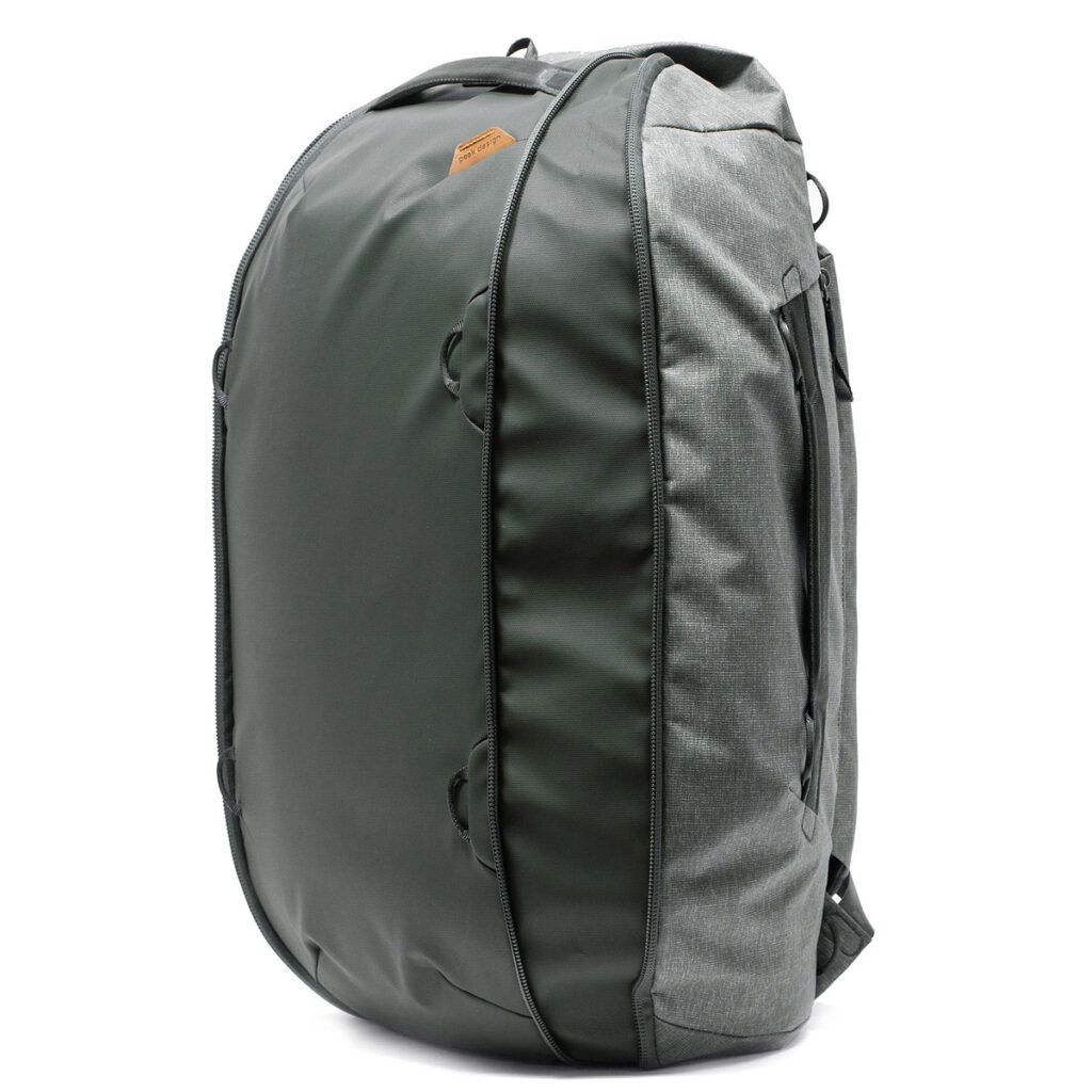 Peak-Design-Travel-Duffelpack-65l-sage-5 Peak Design Travel Duffelpack 65L Sage -repussa on puolijäykkä etukuori, sivukahvat ja useita vetoketjuja, ja se on kuvassa pystyssä valkoisella pohjalla.