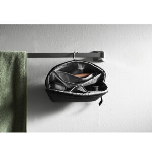 Peak-Design-Wash-Pouch-Small-Black5 Peak Design Wash Pouch Small -pesupussi, musta, roikkuu auki metallisessa pyyhetelineessä vihreän pyyhkeen vieressä, ja sen sisältä paljastuu järjestäytyneitä lokeroita, joissa on hoitotarvikkeita valkoista kuvioitua seinää vasten.