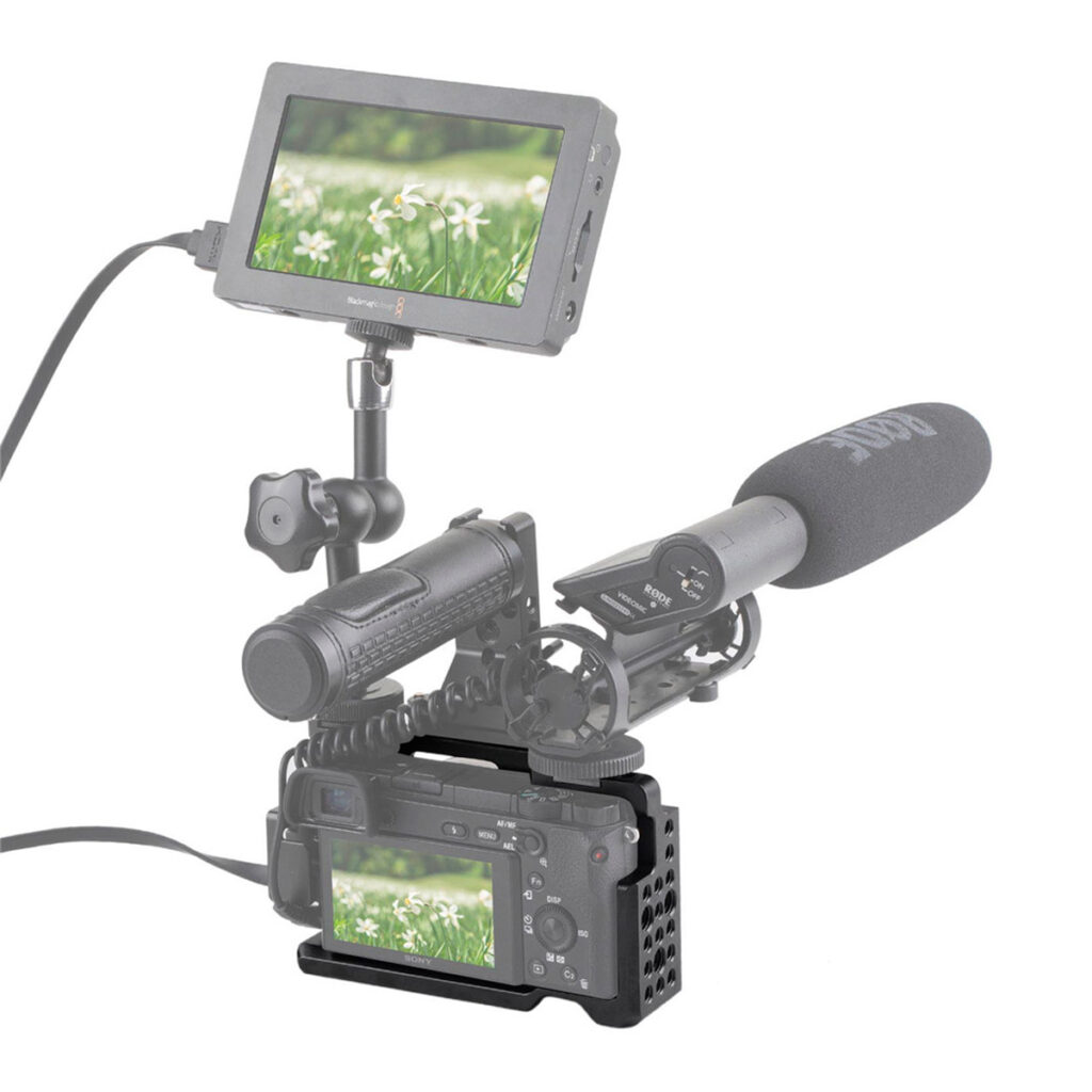 SmallRig-1661-6 SmallRig 1661 Cage -laitteessa oleva Sony A6000 on varustettu ulkoisella mikrofonilla ja monitorilla, ja siinä näkyy lähikuva valkoisista kukista ja ruohosta. Asetelmassa käytetään kaapeleita liitäntöinä ja se on asennettu tukevaan metallitelineeseen.