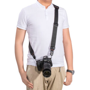 SmallRig-2428-2 Henkilöllä on yllään valkoinen lyhythihainen poolo ja beiget housut, ja hänen olkapäästään lantiolleen roikkuu musta kamera SmallRig 2428 Camera Shoulder Strap -kamerahihnan avulla. Hänen vasen käsivartensa lepää hänen vierellään.