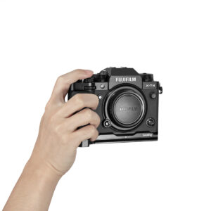 SmallRig-2813-3 Vasemmassa kädessä pidetään Fujifilm X-T4 -kameraa, joka on varustettu SmallRig 2813 L-Shape Grip -kahvalla, objektiivin suojus päällä, valkoista taustaa vasten.