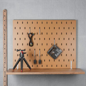 SmallRig-3184-6 Vaaleanharmaaseen seinään on asennettu ruskea SmallRig 3184 Screw & Hex Key Storage Plate, jossa on kelattu kaapeli, kaksi mustaa sovitinta ja kuusiokoloavaimet. Pieni kolmijalka lepää alla olevalla puuhyllyllä.