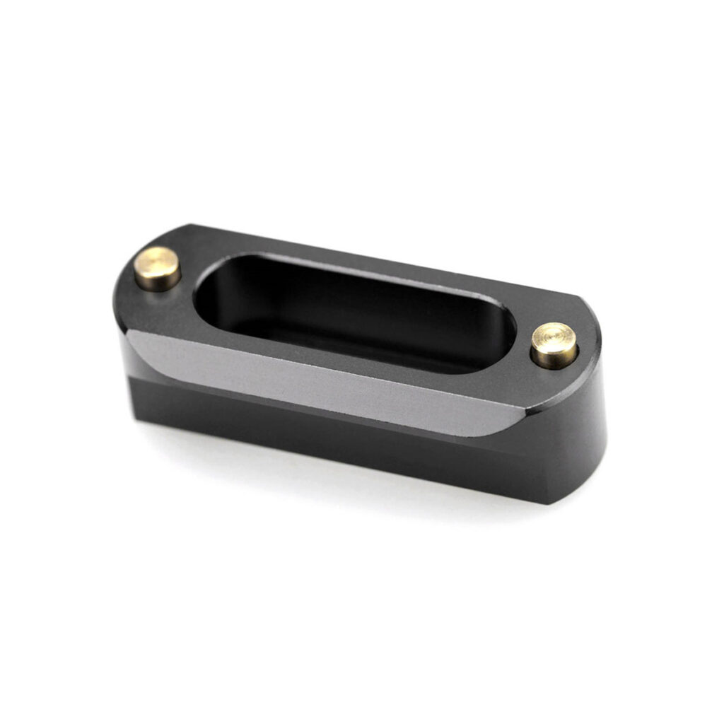 SmallRig-3421-6 SmallRig 3421 Professional Kit Sony A7S III:lle sisältää pienen, soikean mustan metalliosan, jossa on keskellä suorakulmainen ontelo ja kaksi kultaista ruuvia molemmissa päissä, valkoista taustaa vasten.
