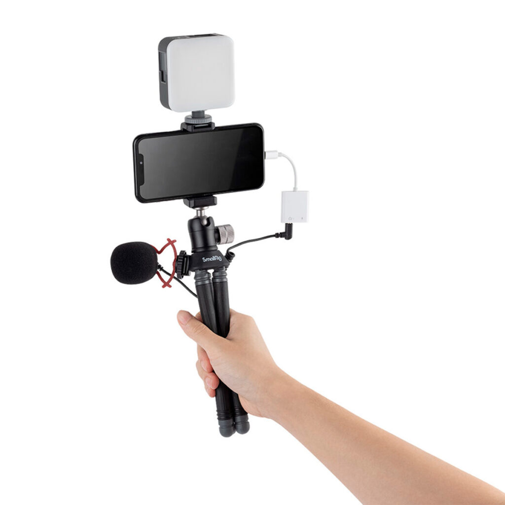 SmallRig-3446-4 Kädessä on SmallRig 3446 BeautyPod 1.5K Flexible Mini Tripod BT-15, jossa on älypuhelin, ulkoinen mikrofoni, valo ja sovitin - kaikki yhdessä kannettava vloggausasetus, joka mahdollistaa videon tallentamisen matkalla.