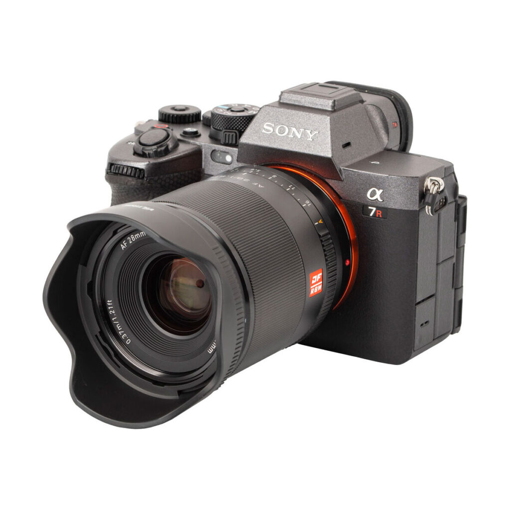 Sony Alpha 7R -peilitön digitaalikamera, jossa on Viltrox AF 28mm f/1.8 -objektiivi Sony E -kiinnikkeelle ja vastavalosuoja kiinnitettynä, kuvattuna valkoista taustaa vasten.