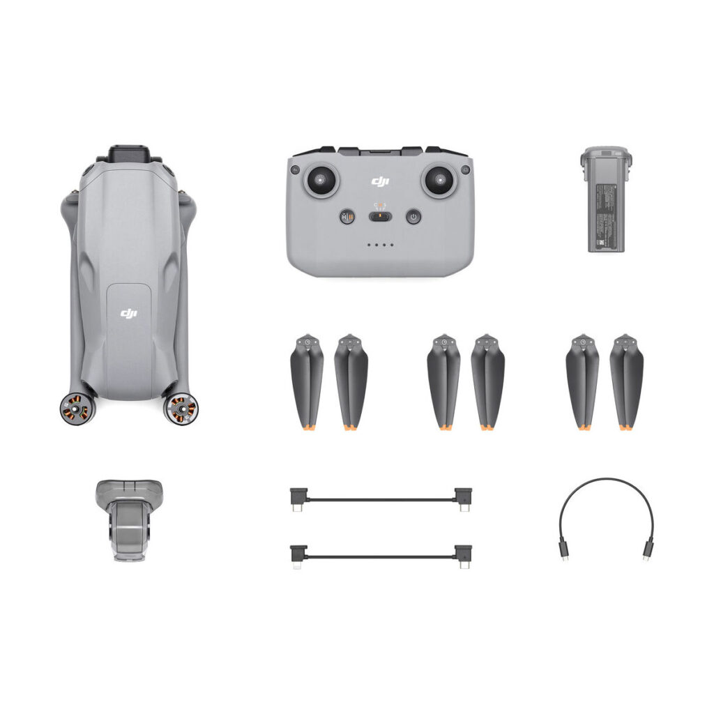 dji_air_3_rc-n2_03 Ylhäältä alas näkymä DJI Air 3 (DJI RC-N2) -pakkauksesta, jossa kokoontaitettu lennokki, kauko-ohjain, neljä potkuria, akku, latauskaapelit, USB-C-kaapeli ja sovitin on järjestetty siististi valkoiselle taustalle.