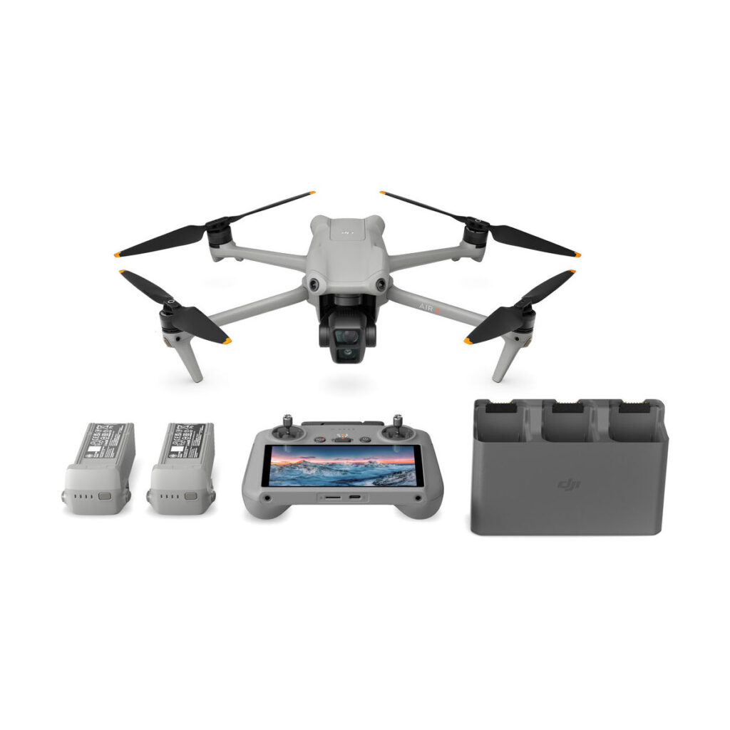 dji_air_3_rc_2_flymore_03 DJI Air 3 (DJI RC 2) Fly More Combo -dronisarja sisältää harmaan nelikopterin, jossa on neljä mustaa potkuria, näytöllä varustetun ohjaimen, kaksi akkua ja kolmella latauspaikalla varustetun latauskeskittimen, joka näkyy valkoisella pohjalla.